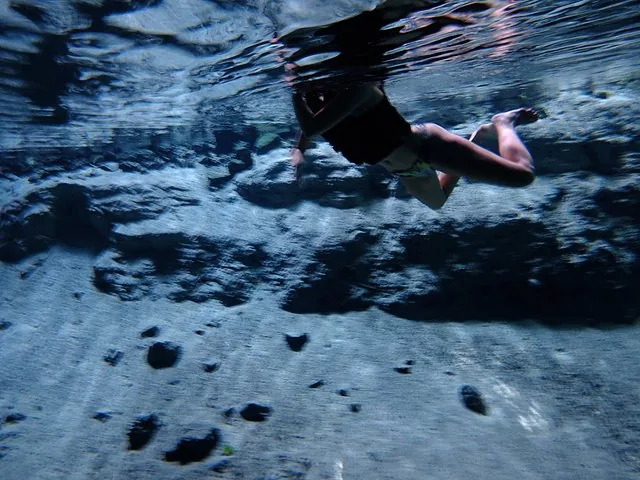 Underwater view of a person snorkeling above the rocky bottom of a cenote.