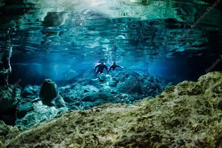 Two divers explore the deep, clear blue waters of Cenote Dos Ojos.