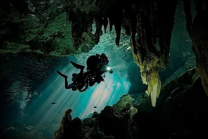 Ein Gerätetaucher schwebt zwischen Lichtstrahlen und Stalaktiten in einer tiefen Cenote.