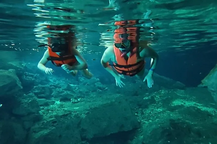 Dos personas hacen esnórquel juntas bajo el agua y exploran las profundidades rocosas de un cenote.
