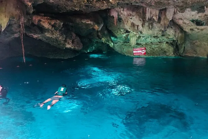 La gente nada en las vibrantes aguas azules del cavernoso Cenote Dos Ojos.